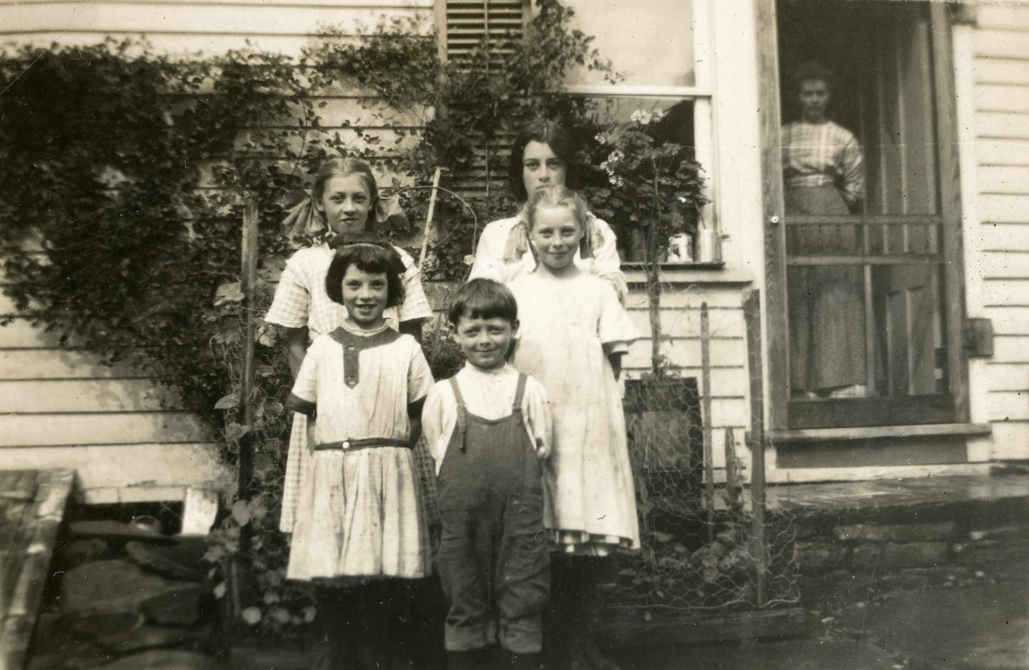 Picture of family, 5 children outside and mother inside